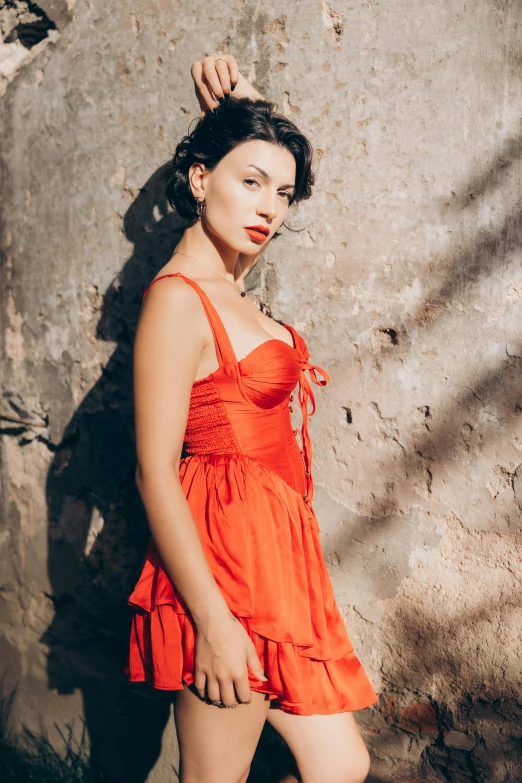 there is a girl in an orange dress and posing against a gray wall
