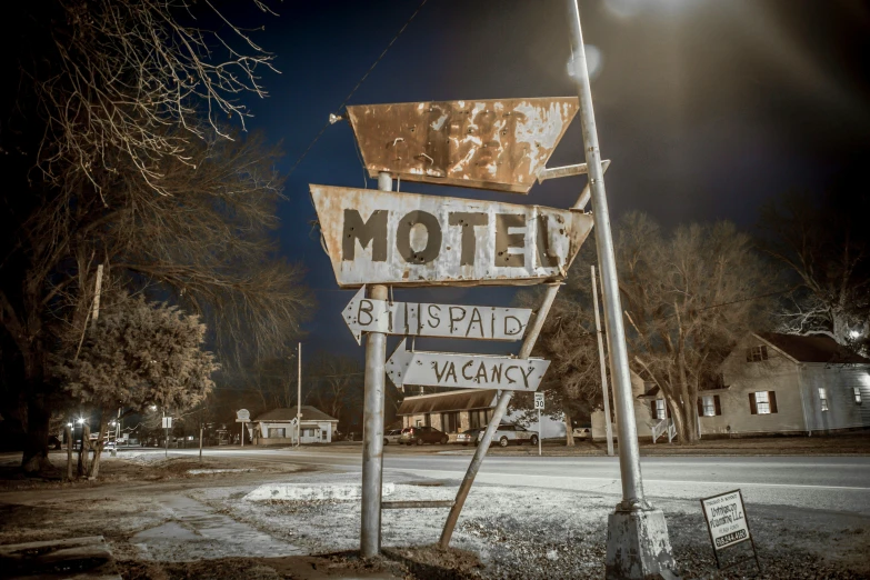 a rusty motel sign standing on the side of the road