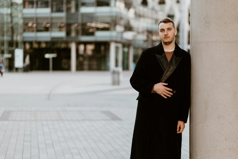 man in black coat leaning against wall on urban city street