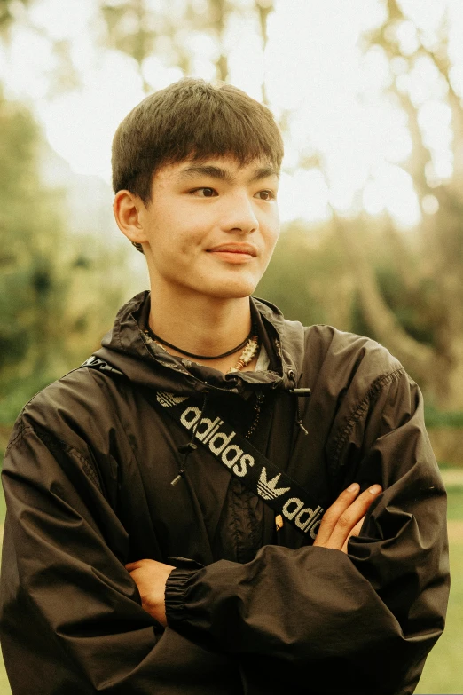 a boy wearing a black jacket stands with his arms folded