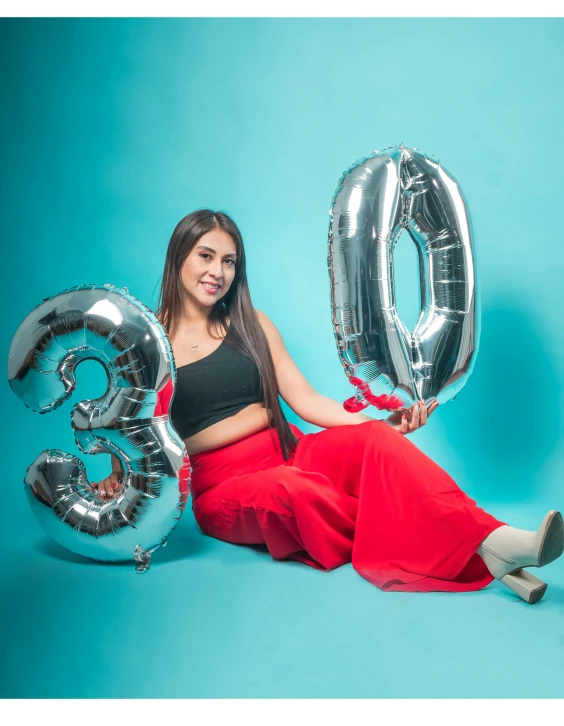 a beautiful young woman holding onto balloons sitting in front of the number three balloon