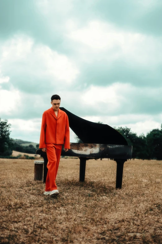 a young man in an orange suit standing next to a black piano