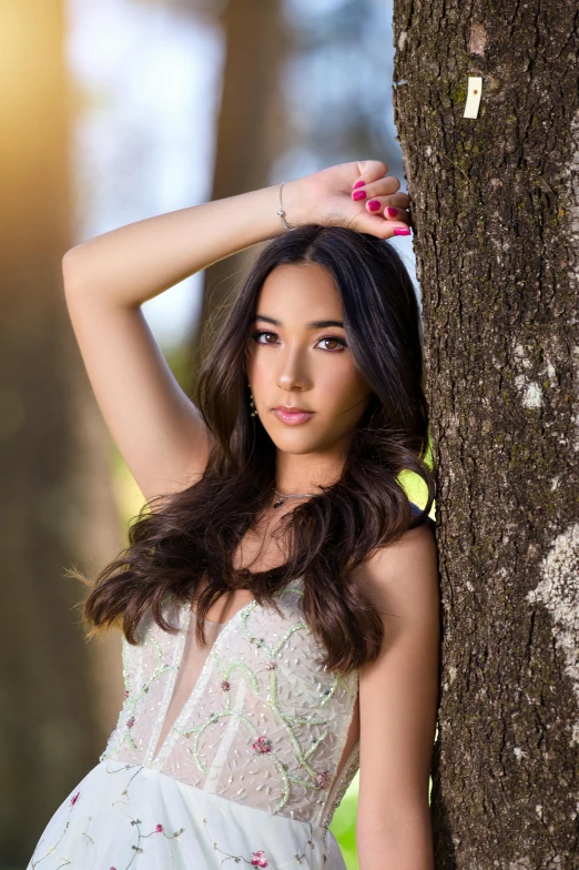 a woman in a white dress standing next to a tree