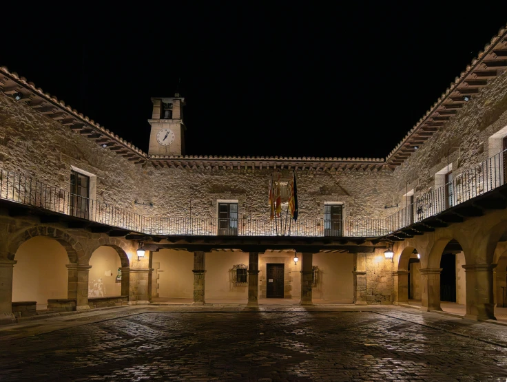 an arched courtyard lit up at night with the building reflecting off its roof