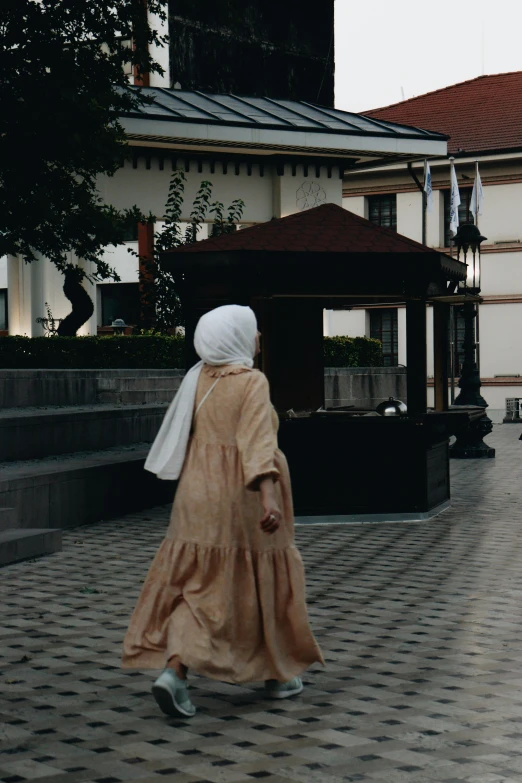 a person walking past a large house with a white scarf on