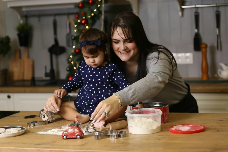 a woman helping a  put dough on top of a wooden table