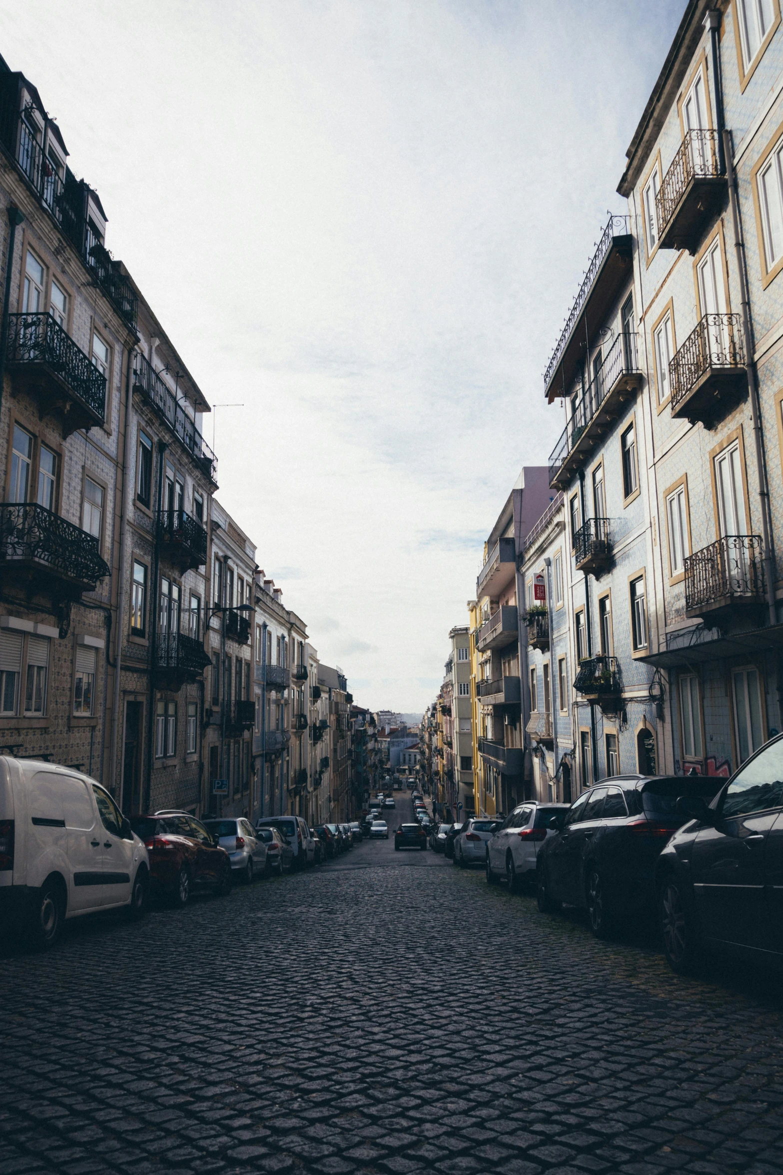 a cobblestone street is lined with parked cars