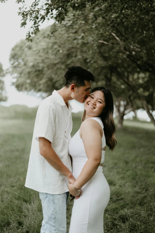 an asian couple cuddle in the grass under a tree