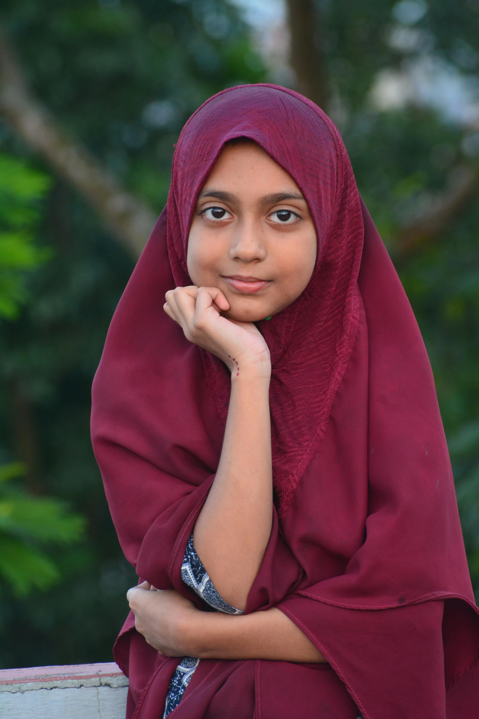 young person wearing a maroon cloth in front of trees