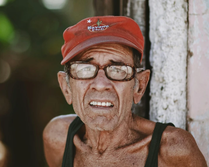 an old man wearing glasses and a hat smiles