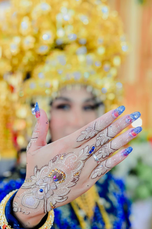 closeup of the hands and face of a woman in a ceremonial costume, in front of a decorated wall