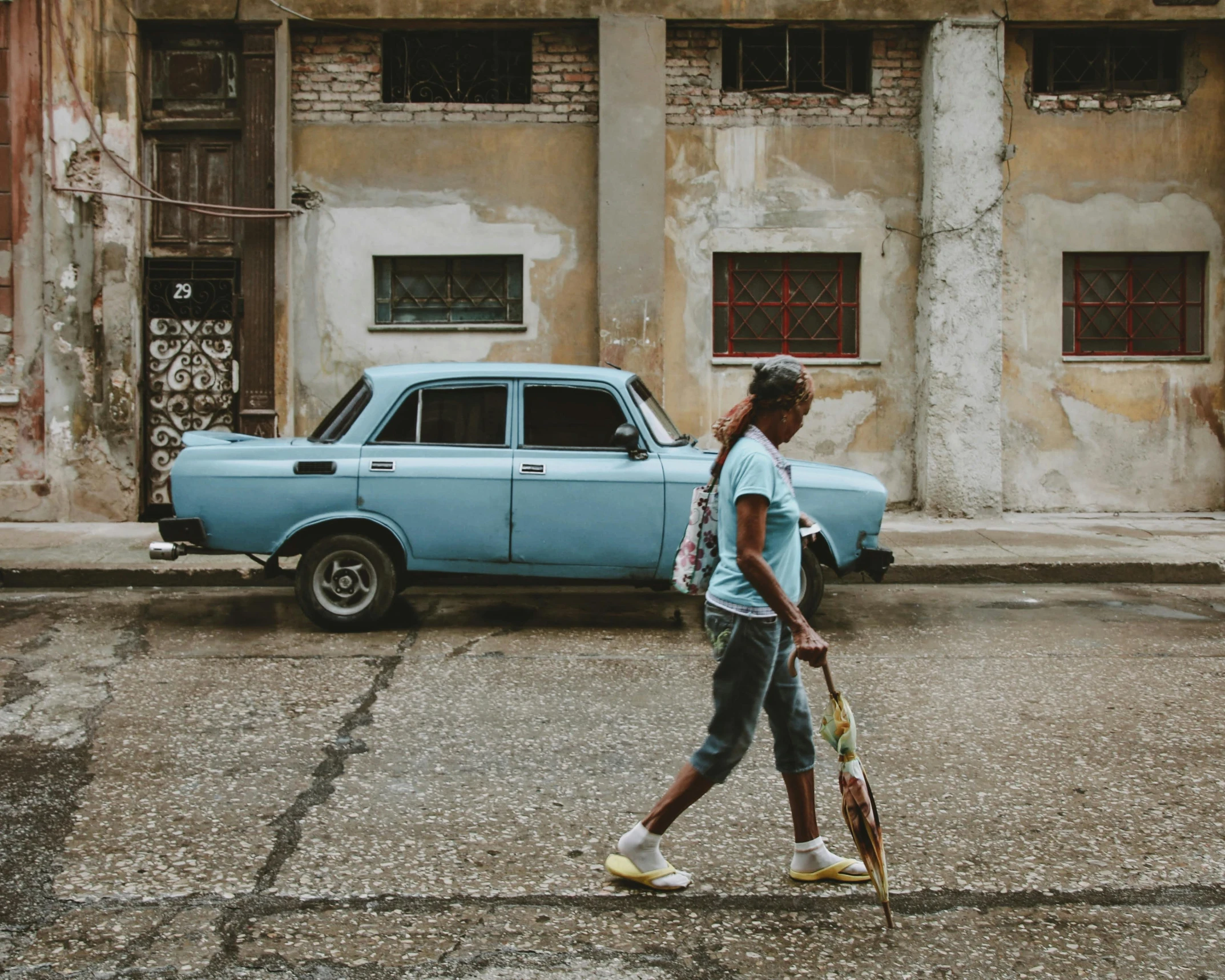 girl with crutches walking by a blue car in front of old building