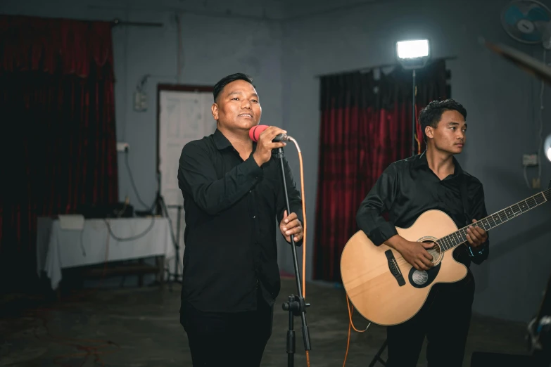 two men singing into a microphone while playing guitar