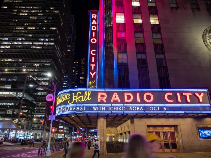 the radio city sign is lit up and people walk by