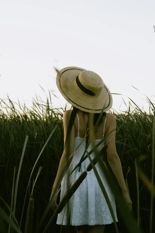 a young woman in a white dress and straw hat walks through tall grass