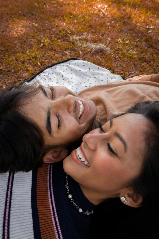 a smiling couple laying in the grass under an umbrella