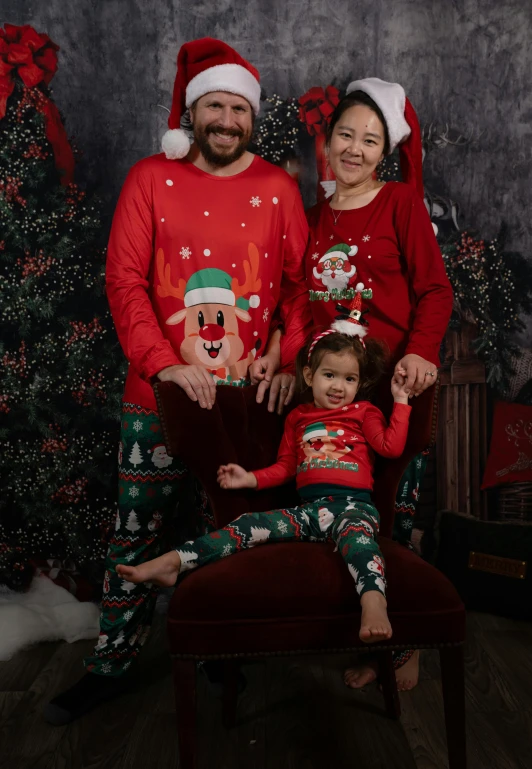 man and woman in matching christmas pajamas sitting next to a toddler