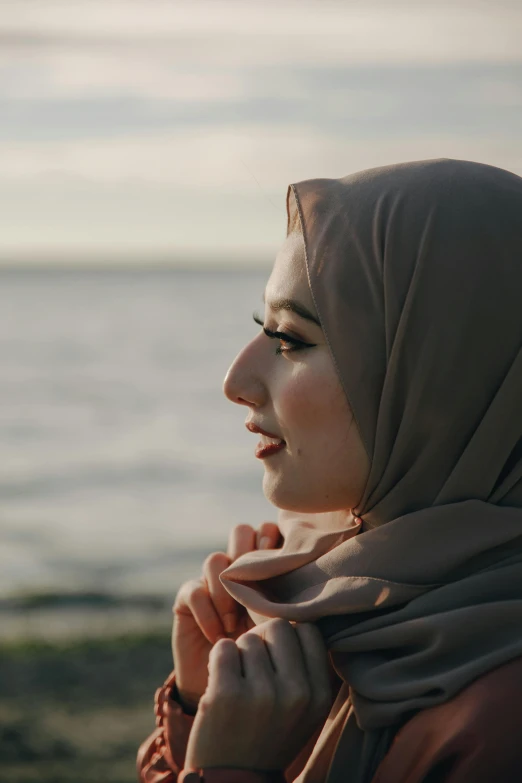 a woman standing next to the ocean wearing a headscarf