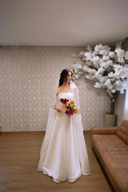 a bride with a dress and flowers standing in front of a sofa