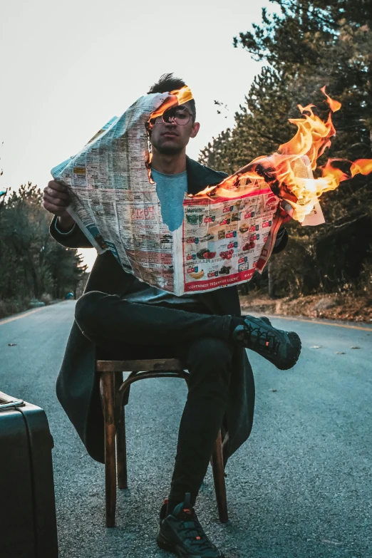 man sitting on chair holding soing burning outside