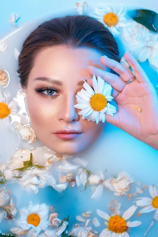 a girl lying in water with daisy petals on her finger