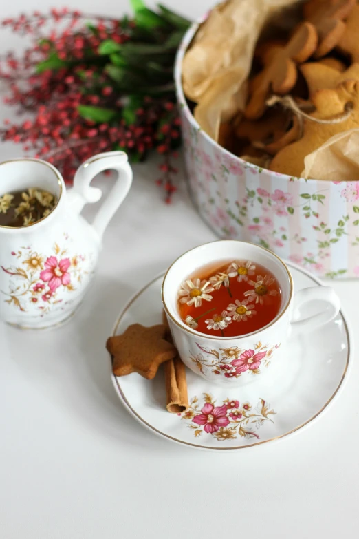 a tea cup and saucer are beside a cookie tin