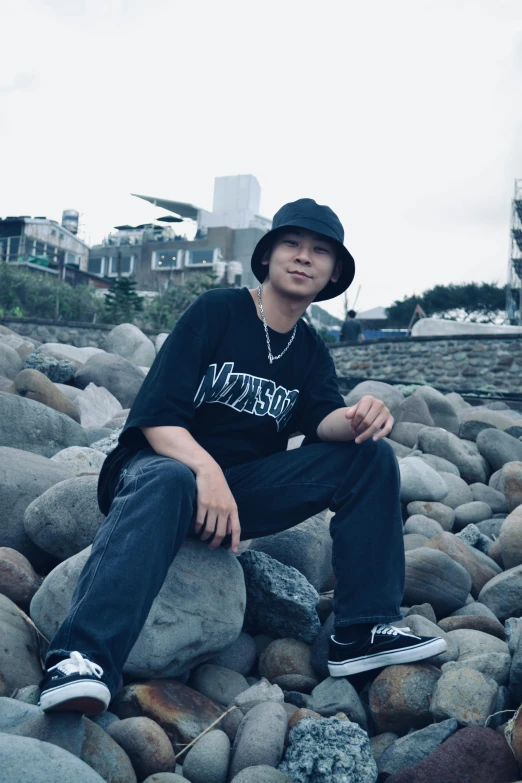 a young man sitting on rocks wearing a hat