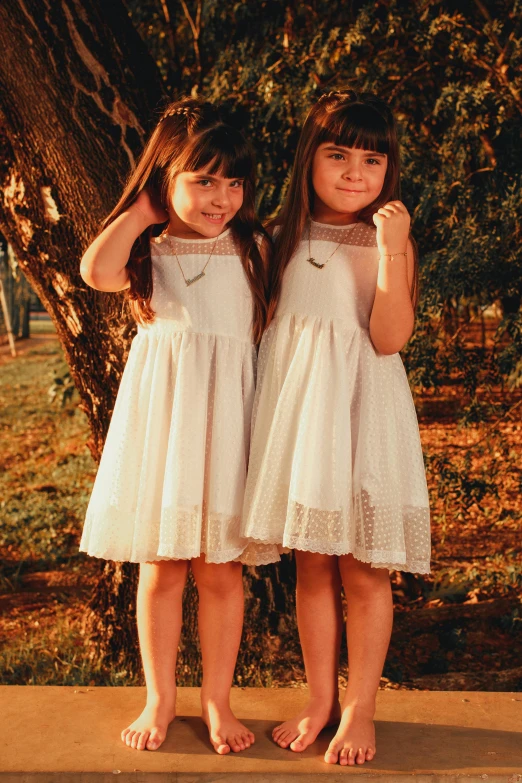 two little girls standing near a tree in their dresses