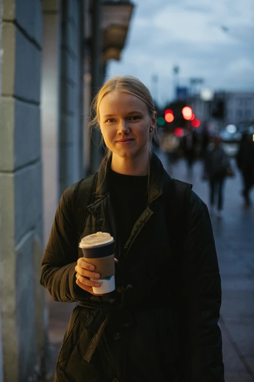 a woman standing on the sidewalk and drinking from a cup