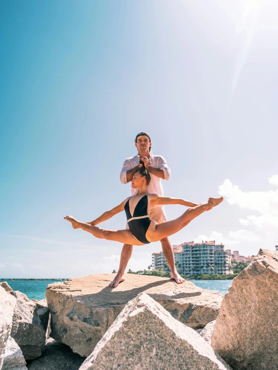 man and woman in bathing suits doing a aerial leap on rocks