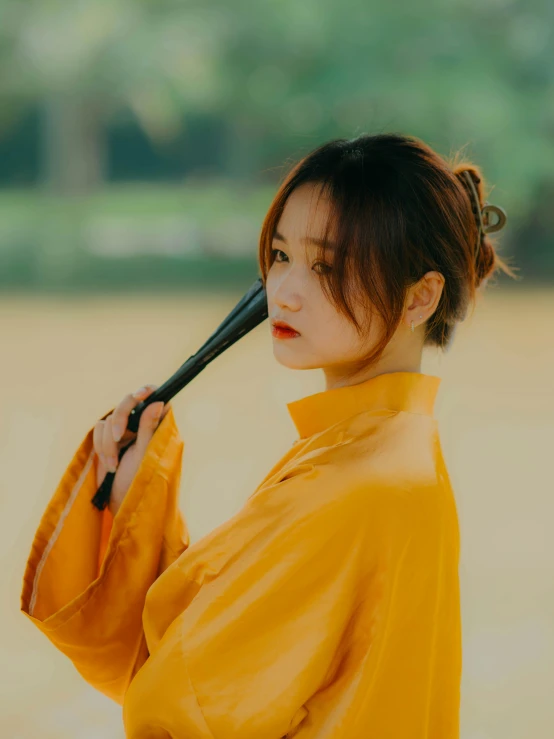 a woman with a fan and a orange outfit holds a black umbrella