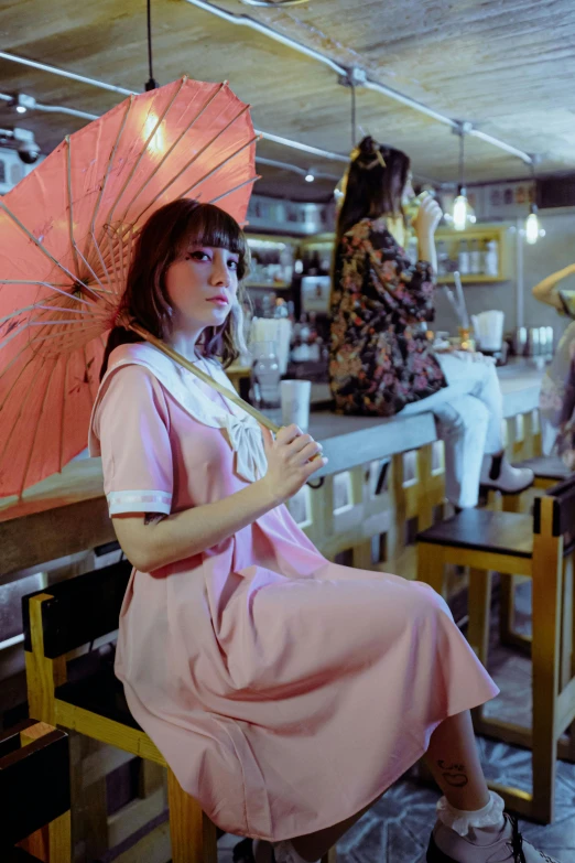 a woman sits on a stool while holding an umbrella