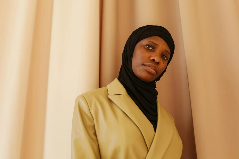 a woman wearing a jacket and scarf is standing against a curtain