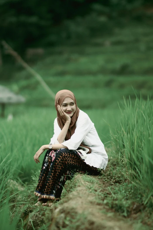 a young woman sitting in the grass with a bird in the distance