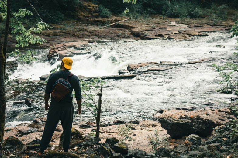 a man standing at the edge of a river with a book bag