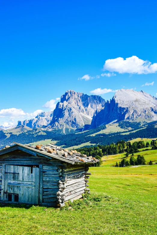 small shack in the middle of a grassy field with mountains and grass on either side