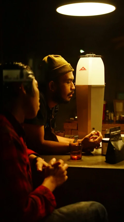 two men sitting at a table with a phone and drink