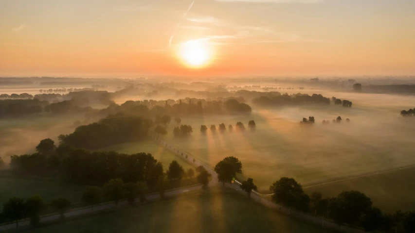 the sun rising over trees and fields in an area covered by mist