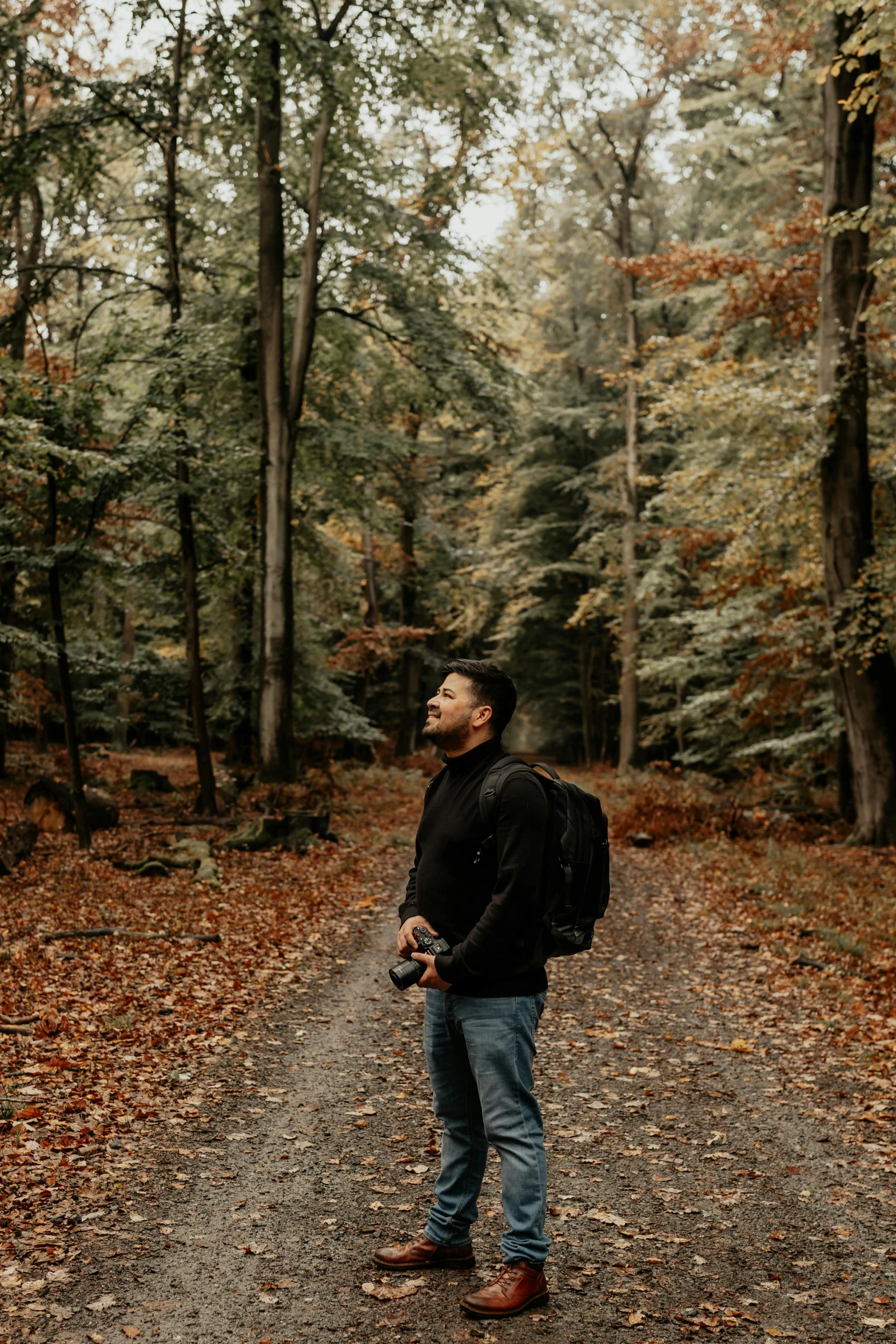 a man stands on a forest path looking up to the sky