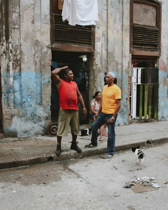 men outside of an old dilapidated building with a cat on the ground