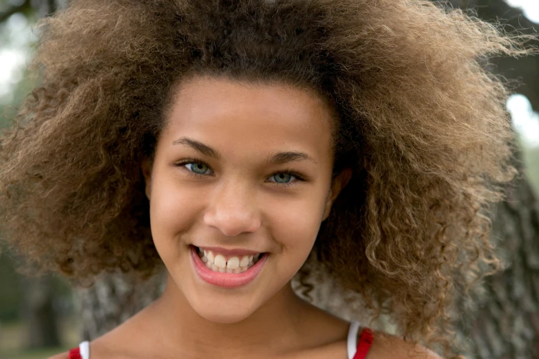 a smiling woman with an afro is by a tree