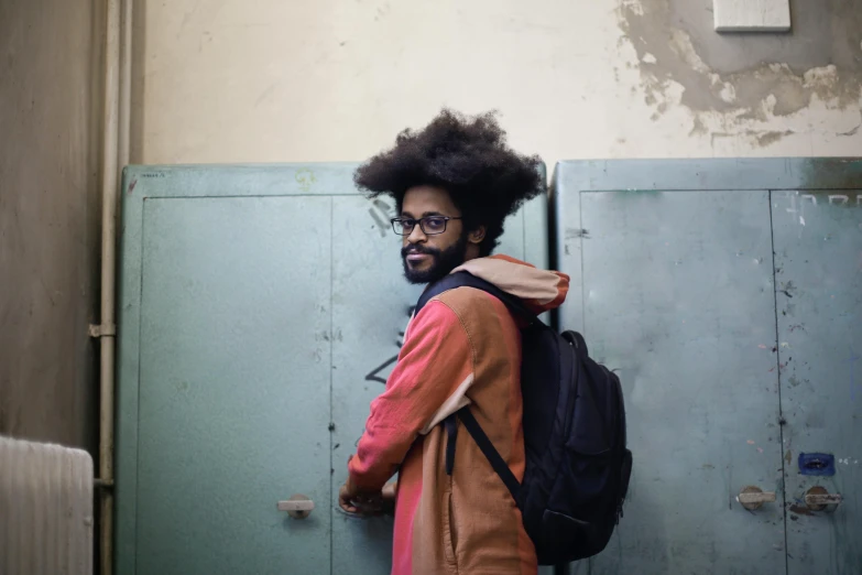 man with large afro in orange jacket and black backpack