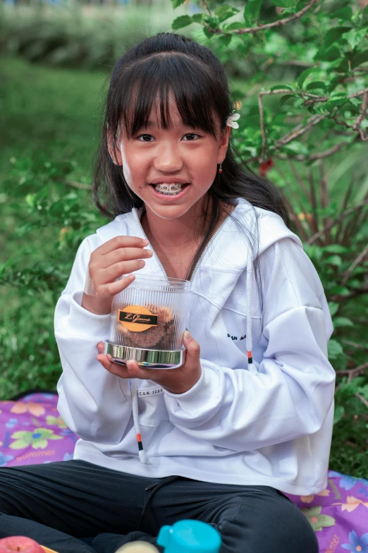 a girl in white jacket sitting down holding a jar