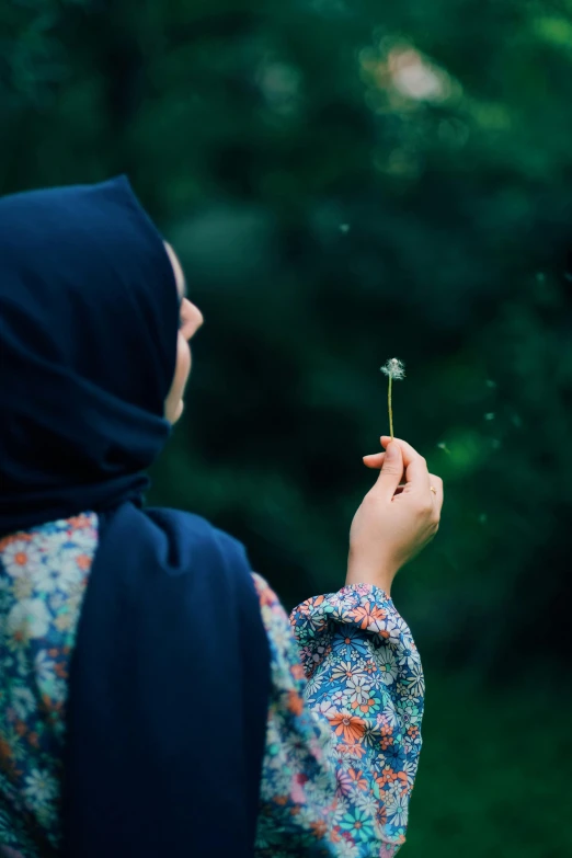 a woman wearing a headscarf is looking at a flower