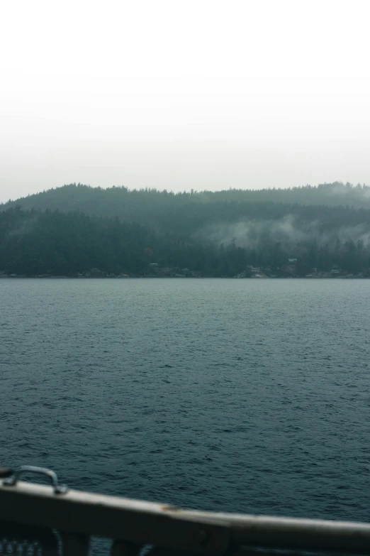 a foggy mountain over water with trees on the side