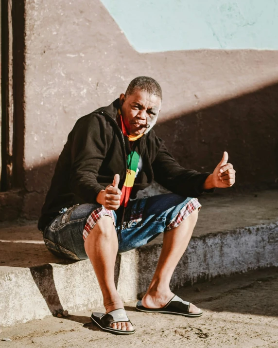 a young man is sitting on a curb giving a thumbs up