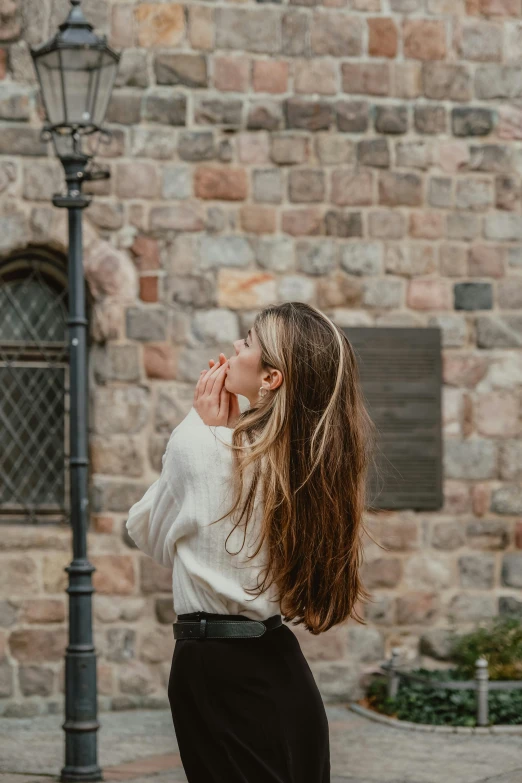 a woman with long hair leaning against a light pole on a brick wall