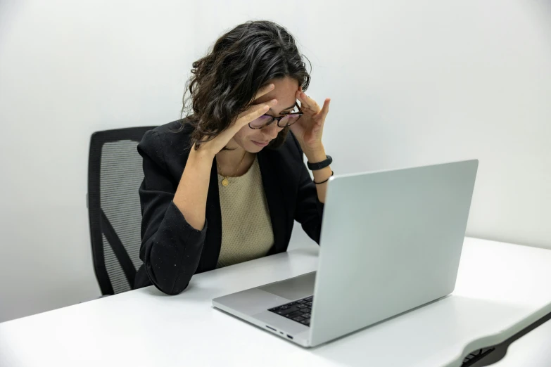 woman at desk looking exhausted while using laptop computer