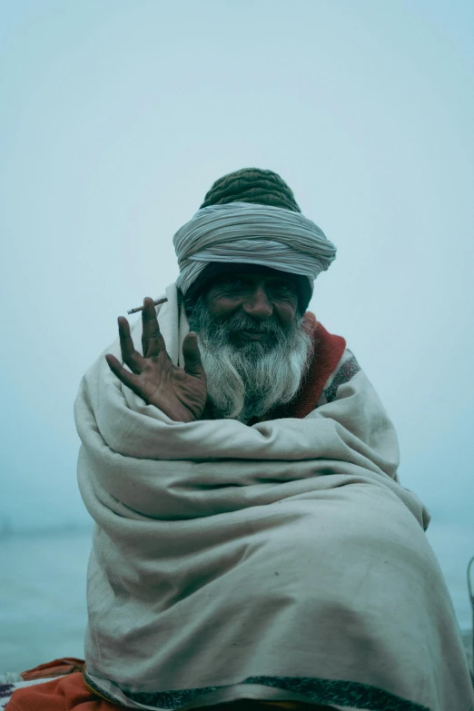 a man wearing a blanket sits near the ocean