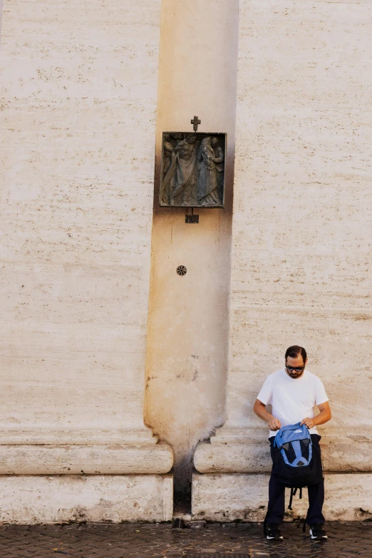 a man with a backpack and a bag sitting in front of a cross